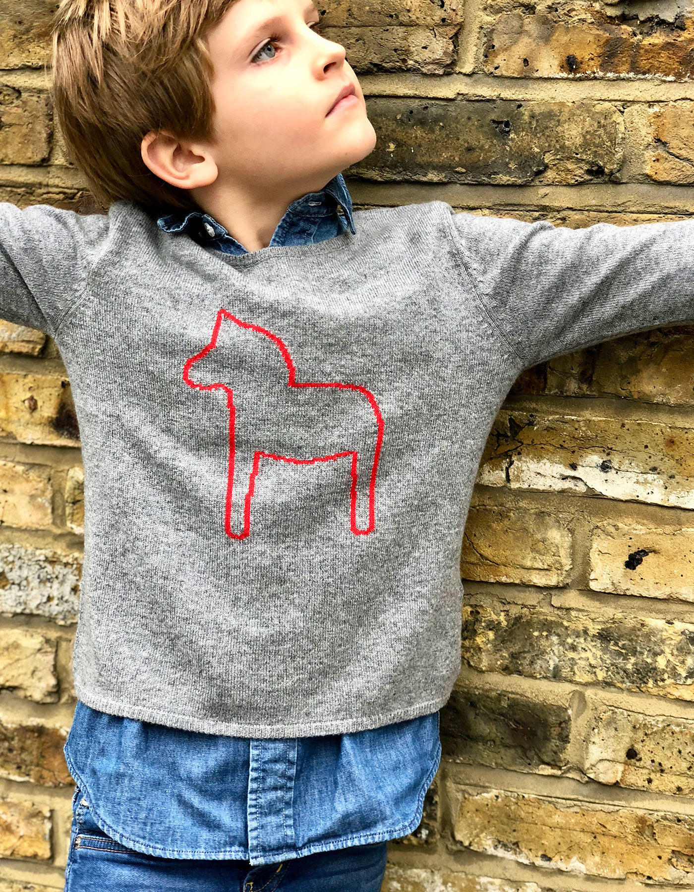 A young boy wearing a kids designer cahsmere jumper over denim shirt and jeans.