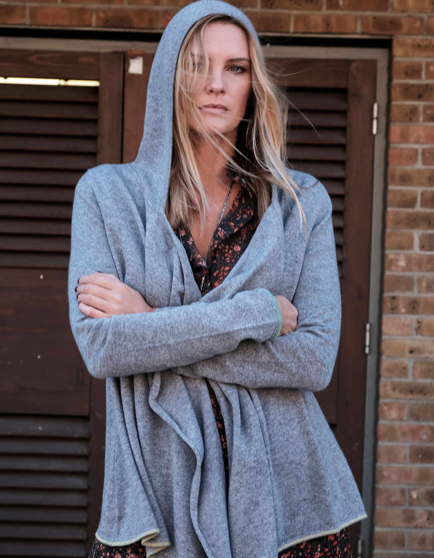 Woman standing in front of louvre doors, arms folded, wearing a designer cashmere hoody.