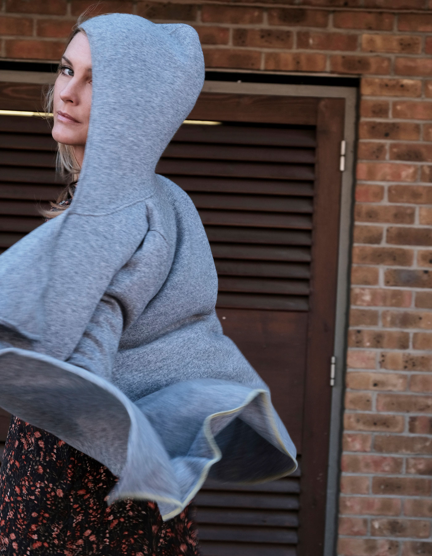 Action shot of a woman in a tie hooded cashmere jumper by Malin Darlin, her clothing blowing toward the camera.