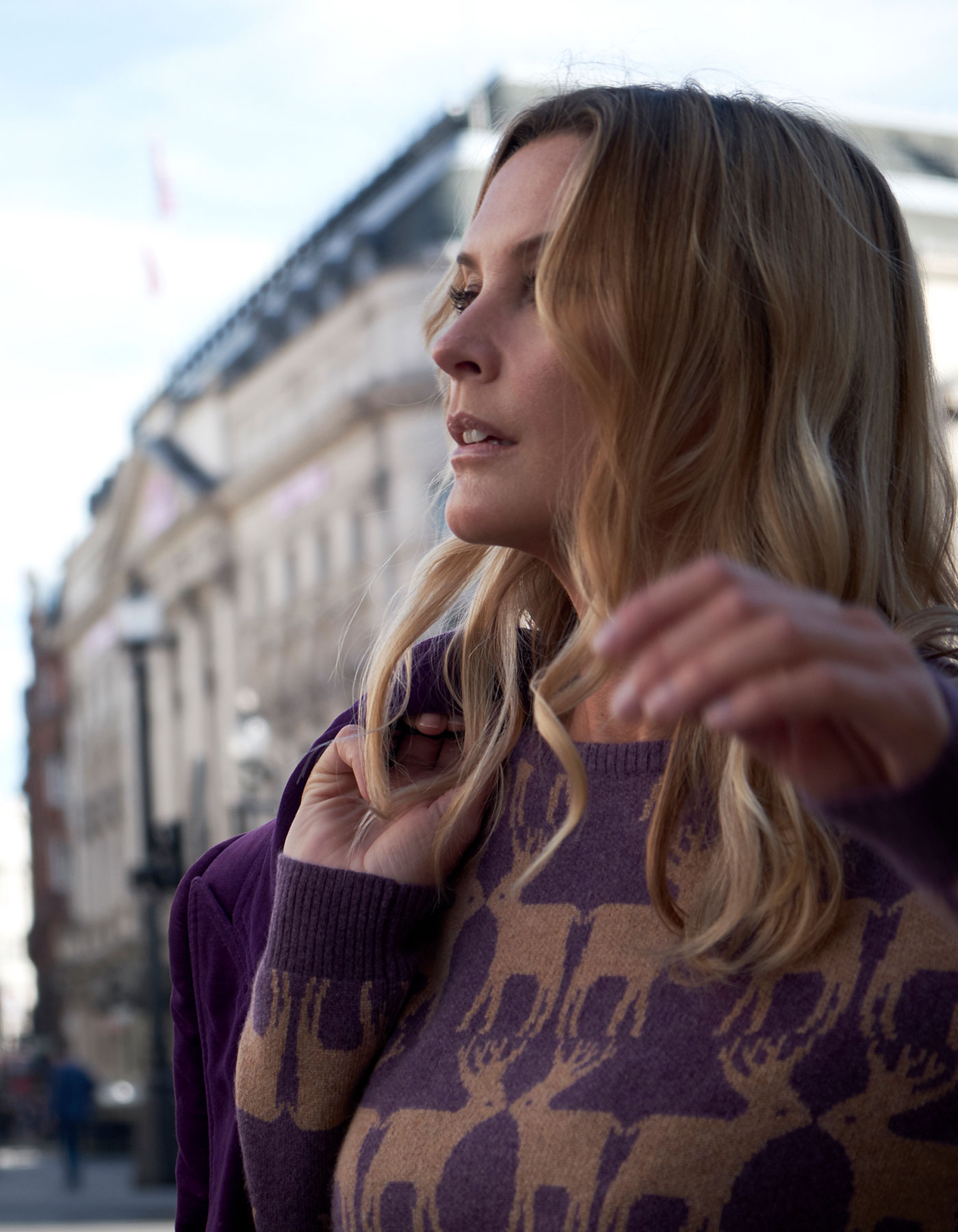 Close up of a woman in a city wearing cashmere knitwear, the malin darlin Reindeer purple cashmere jumper.