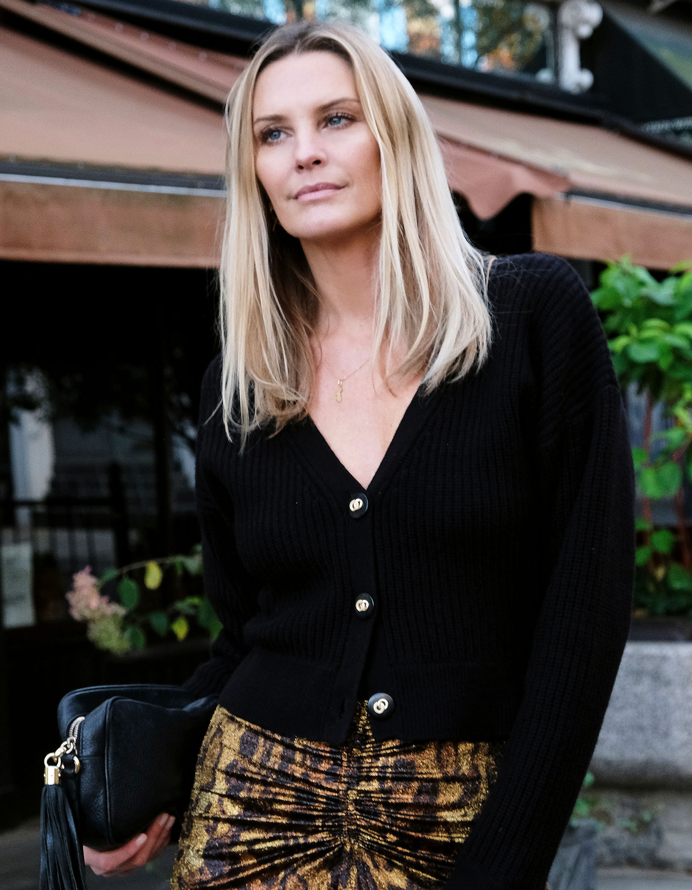 The malin darlin Coco rib cardigan, a black wool cashmere cardigan, worn by a model standing outside a restaurant.