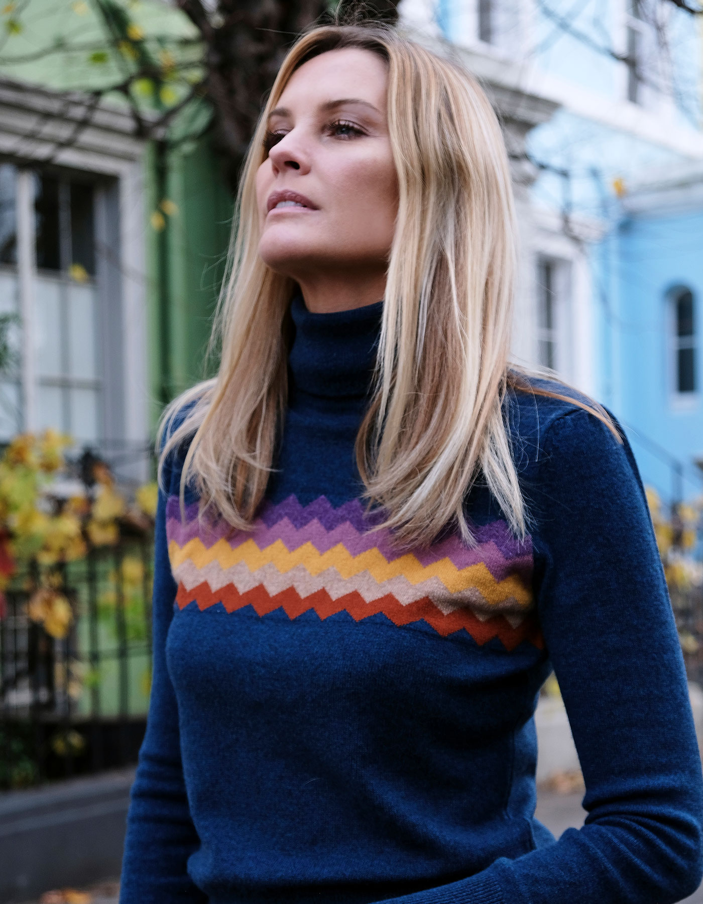 A woman wearing malin darlin cashmere knitwear, the Zigzag Blue cashmere jumper, with houses in the background.